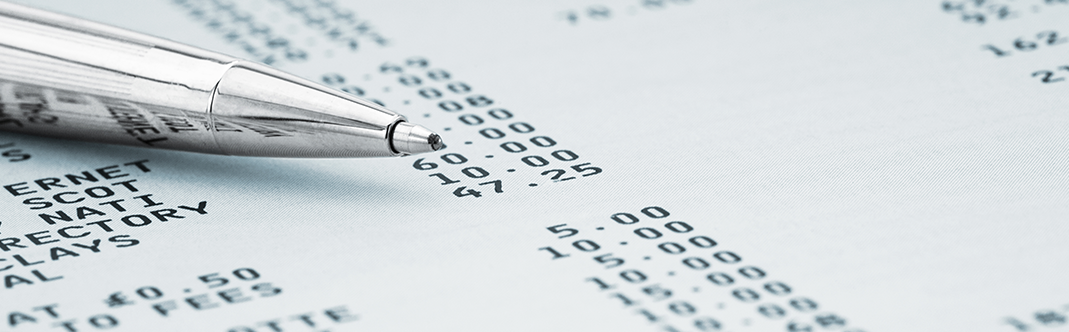 A close-up of a silver pen on a financial document showing detailed expenses and costs