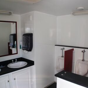 Interior of a clean portable restroom trailer with two sinks, a large mirror, soap dispensers, and three urinals against a white wall