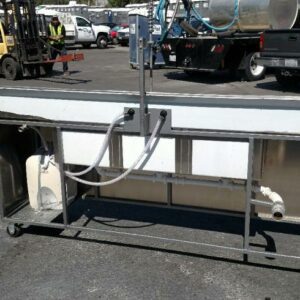 Back view of a portable 3-compartment sink with a 3-gallon water heater and a 250-gallon waste tank, located in a busy outdoor area with other utility vehicles.